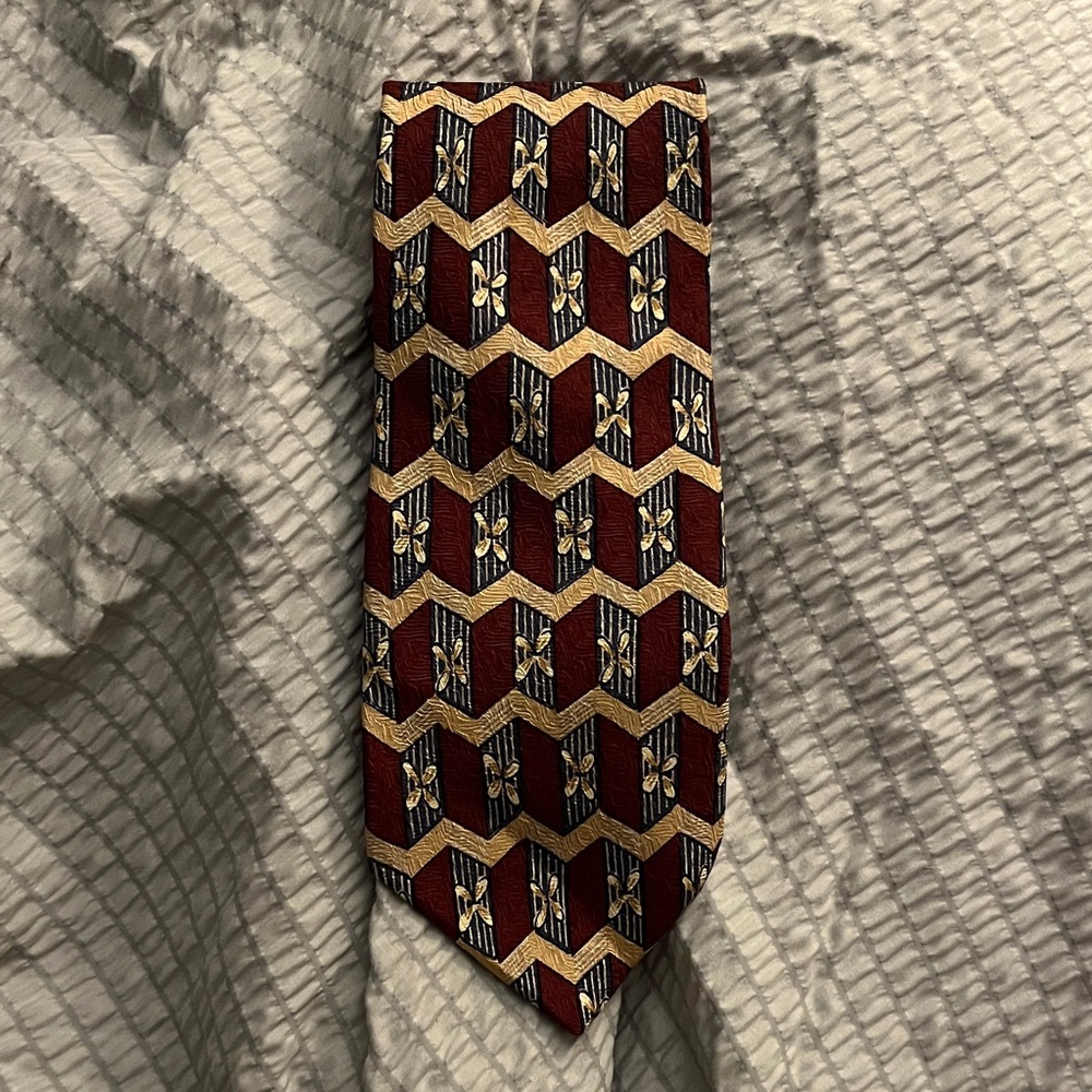 Tom James 100% silk necktie with a red, blue, and gold geometric pattern.